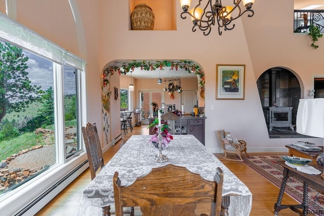 dining room with a wood stove, a notable chandelier, baseboard heating, and light hardwood / wood-style floors