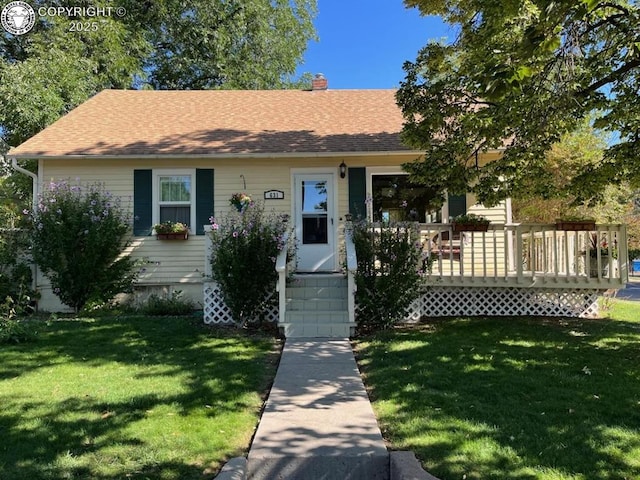 view of front facade featuring a shingled roof, a chimney, a wooden deck, and a front yard