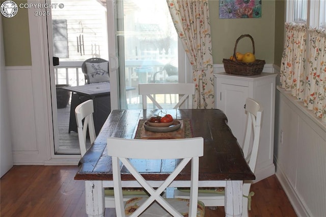 dining space with a wainscoted wall, a decorative wall, and dark wood-type flooring