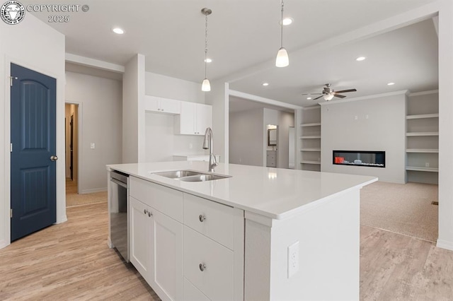 kitchen with a glass covered fireplace, light wood-style floors, built in shelves, white cabinetry, and a sink