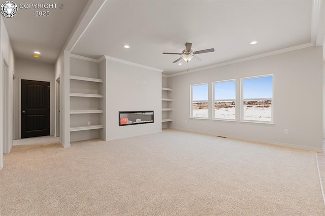 unfurnished living room with carpet floors, built in shelves, baseboards, and a glass covered fireplace