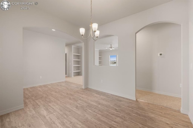 unfurnished room with built in features, arched walkways, light wood-style flooring, and ceiling fan with notable chandelier