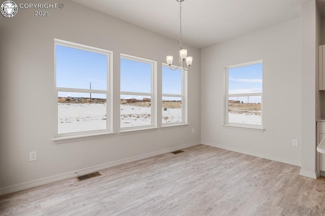 empty room featuring light wood finished floors, baseboards, visible vents, and a notable chandelier