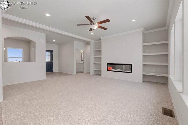 unfurnished living room with baseboards, a glass covered fireplace, ornamental molding, carpet floors, and built in shelves