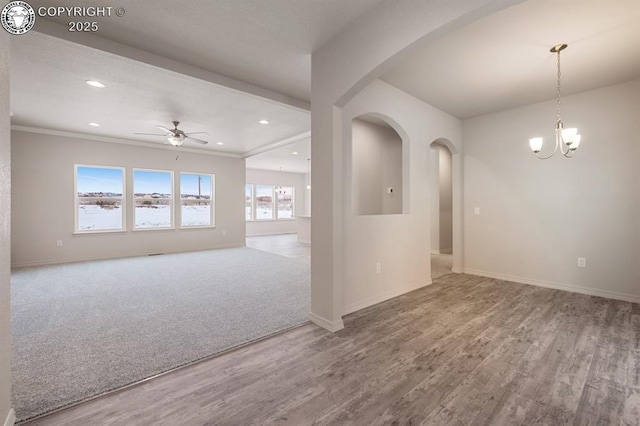 unfurnished room with ceiling fan with notable chandelier, arched walkways, baseboards, and wood finished floors