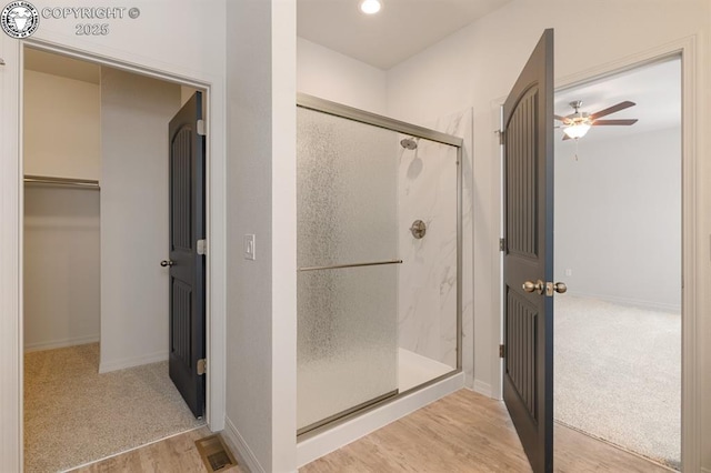 full bathroom featuring wood finished floors, a ceiling fan, visible vents, a shower stall, and a walk in closet