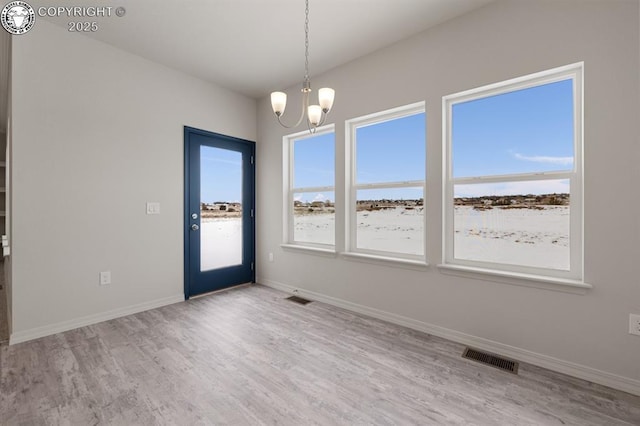 unfurnished room featuring an inviting chandelier, wood finished floors, visible vents, and baseboards