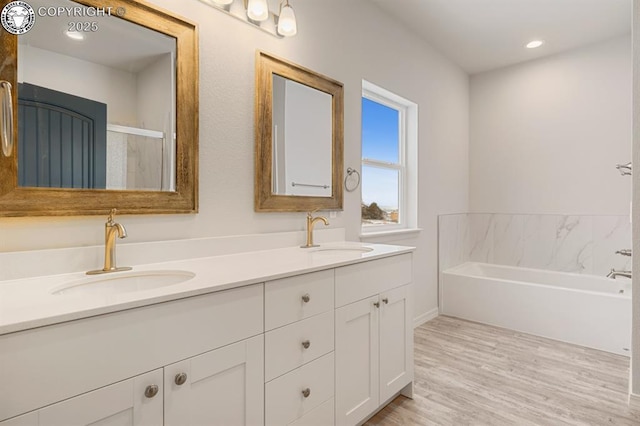 full bath with wood finished floors, a sink, a bath, and double vanity