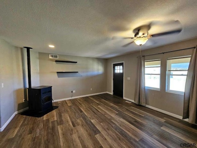 unfurnished living room featuring dark hardwood / wood-style flooring, ceiling fan, a textured ceiling, and a wood stove