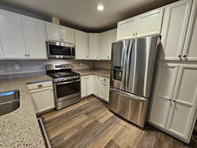 kitchen with sink, dark wood-type flooring, appliances with stainless steel finishes, white cabinetry, and light stone countertops