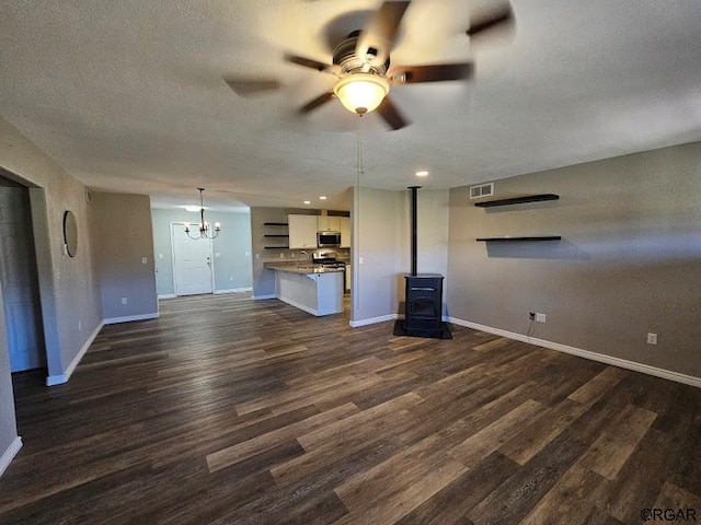 unfurnished living room featuring dark hardwood / wood-style flooring, ceiling fan with notable chandelier, a textured ceiling, and a wood stove