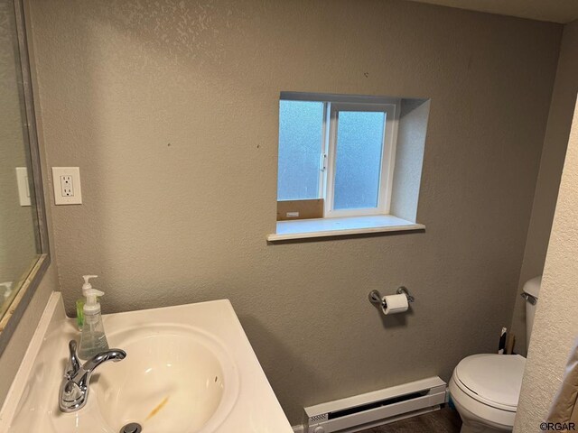 bathroom with sink, wood-type flooring, toilet, and baseboard heating