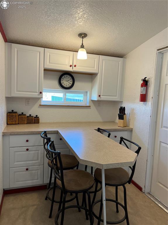 5105 Electric Ave, Westcliffe, CO 81252 - kitchen with white cabinetry, a textured ceiling, light countertops, a breakfast bar, and a peninsula