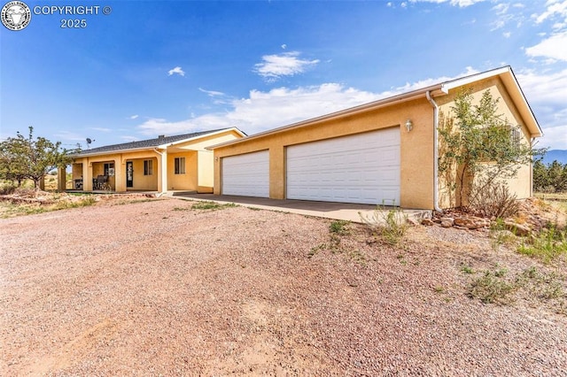 ranch-style home featuring covered porch, driveway, an attached garage, and stucco siding