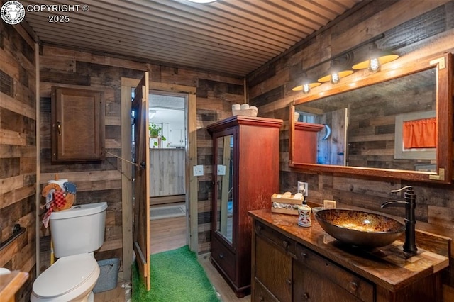 bathroom with vanity, toilet, and wood walls