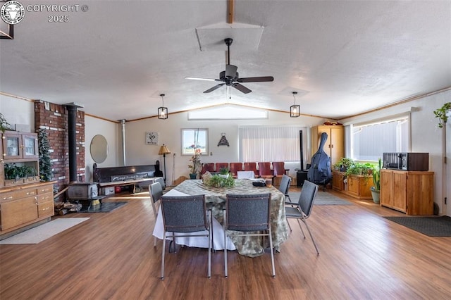 dining area featuring ceiling fan, lofted ceiling, wood-type flooring, and a wood stove