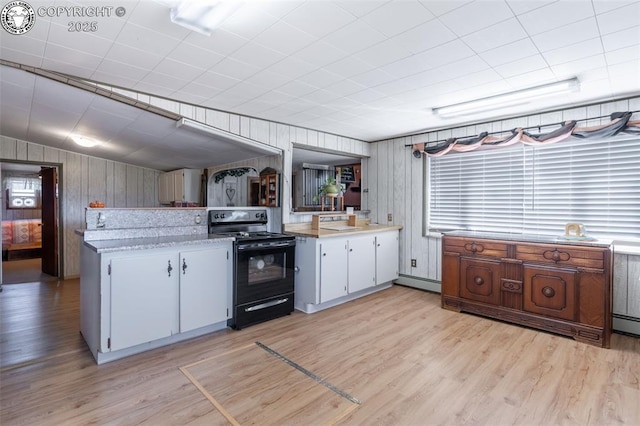 kitchen featuring white cabinetry, black / electric stove, light hardwood / wood-style flooring, and wooden walls