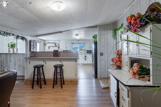 kitchen with light hardwood / wood-style flooring, a breakfast bar, appliances with stainless steel finishes, white cabinetry, and kitchen peninsula