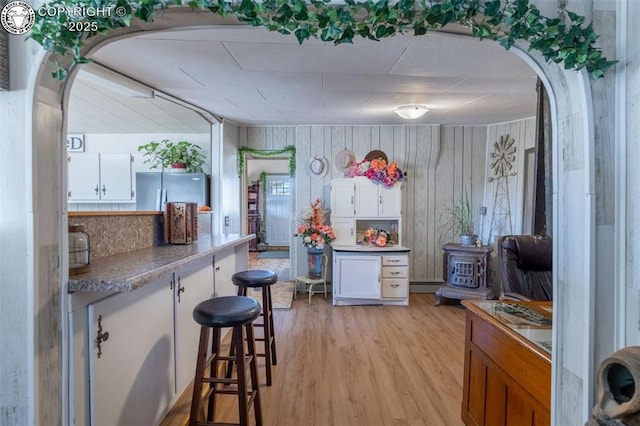 kitchen with light hardwood / wood-style flooring, a baseboard radiator, stainless steel refrigerator, and white cabinets