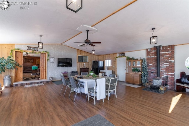 dining space featuring vaulted ceiling, wood walls, a wood stove, dark hardwood / wood-style flooring, and ceiling fan