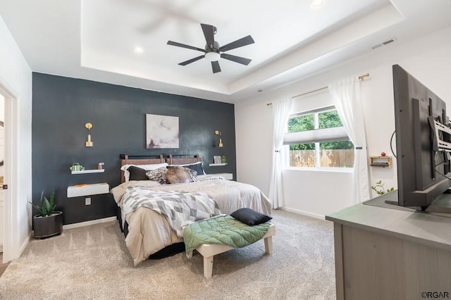 carpeted bedroom with a raised ceiling and ceiling fan