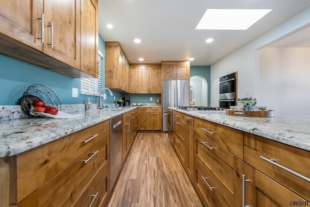 kitchen featuring appliances with stainless steel finishes, sink, light stone counters, and light hardwood / wood-style floors