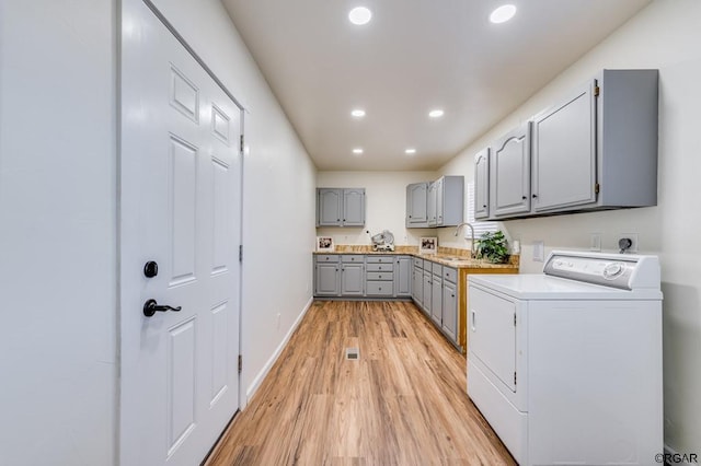 laundry area featuring cabinets, washer / dryer, sink, and light hardwood / wood-style flooring