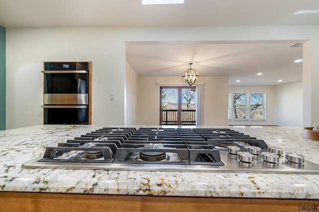 interior details featuring pendant lighting, stainless steel appliances, a chandelier, and light stone counters