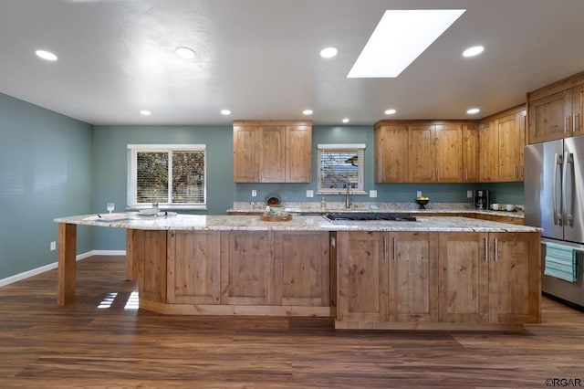 kitchen with dark hardwood / wood-style flooring, a kitchen island, stainless steel fridge, and light stone counters