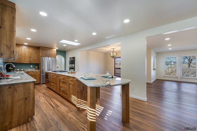 kitchen with sink, dark wood-type flooring, stainless steel appliances, a center island, and light stone counters