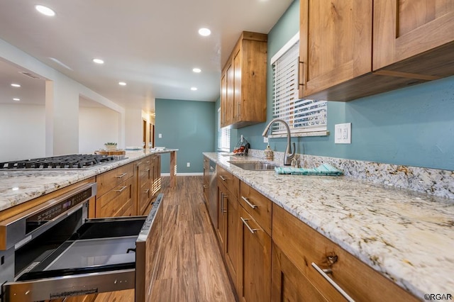 kitchen with sink, hardwood / wood-style floors, light stone counters, wall oven, and stainless steel gas cooktop