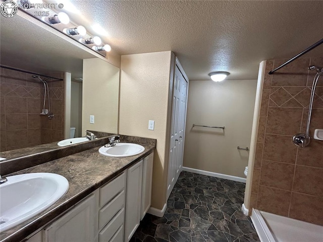 7465 Sun Prairie Dr, Colorado Springs, CO 80925 - full bathroom with double vanity, tiled shower, a textured ceiling, and stone finish floors