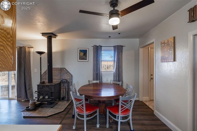 dining room featuring a wood stove, baseboards, a ceiling fan, and wood finished floors