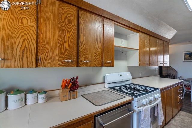 kitchen with brown cabinets, light countertops, stainless steel dishwasher, and white gas range oven