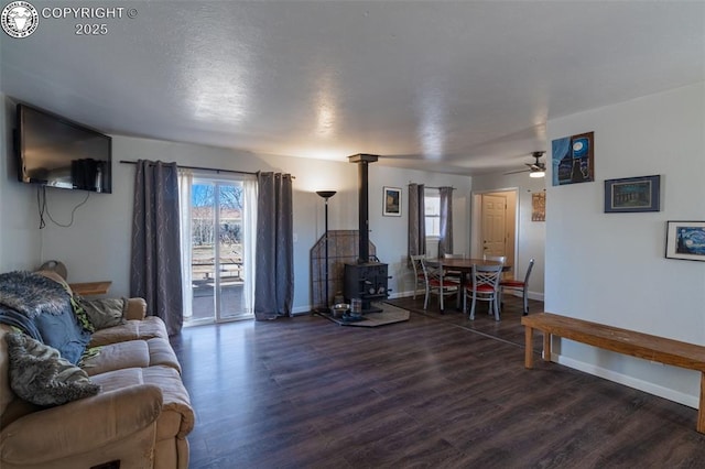 living area with dark wood-style floors, ceiling fan, a wood stove, and baseboards