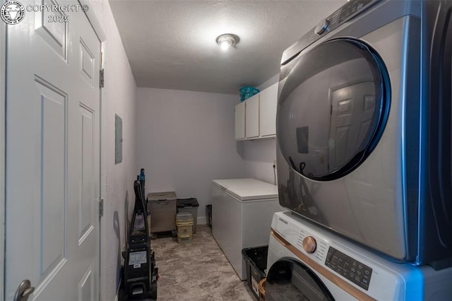 laundry area with stacked washer / dryer, cabinet space, and a textured ceiling