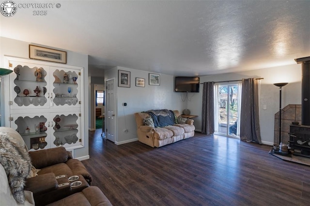 living room with a textured ceiling, wood finished floors, a wood stove, and baseboards