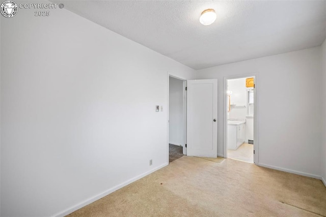 unfurnished bedroom with light colored carpet, a textured ceiling, baseboards, and ensuite bathroom