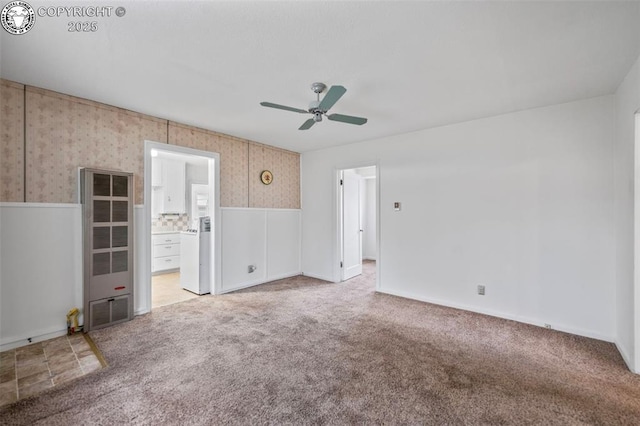 carpeted spare room with wallpapered walls, a ceiling fan, and a wainscoted wall