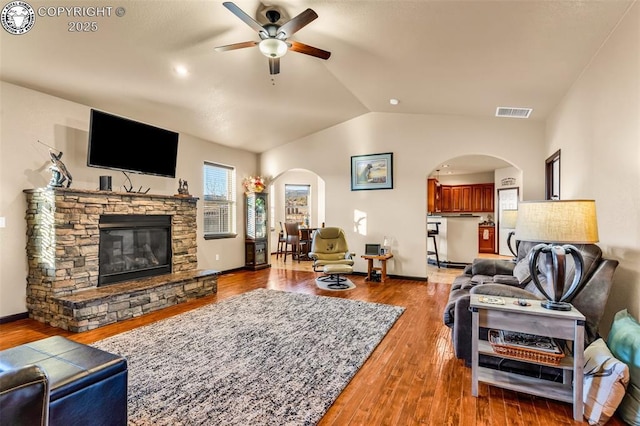 living room featuring ceiling fan, lofted ceiling, wood-type flooring, and a stone fireplace