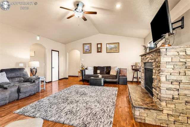 living room featuring hardwood / wood-style flooring, a stone fireplace, ceiling fan, and vaulted ceiling