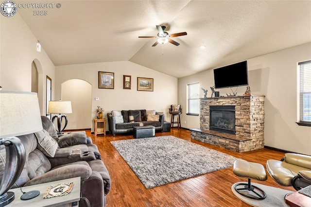 living room featuring hardwood / wood-style flooring, lofted ceiling, a stone fireplace, and ceiling fan