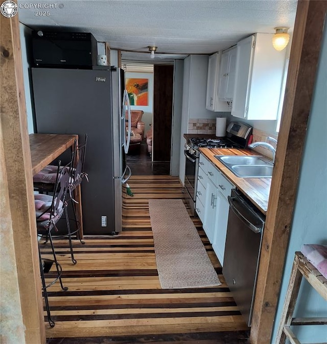 kitchen with sink, appliances with stainless steel finishes, dark hardwood / wood-style floors, white cabinets, and decorative backsplash