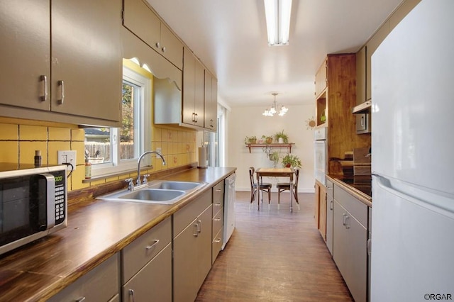 kitchen featuring pendant lighting, sink, decorative backsplash, white appliances, and an inviting chandelier