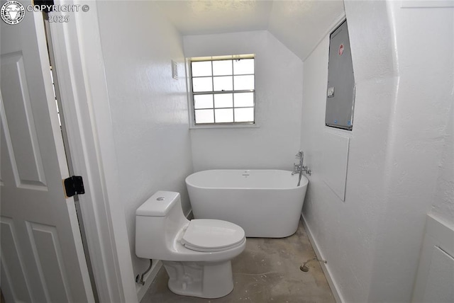 full bath featuring toilet, baseboards, a freestanding bath, concrete floors, and vaulted ceiling
