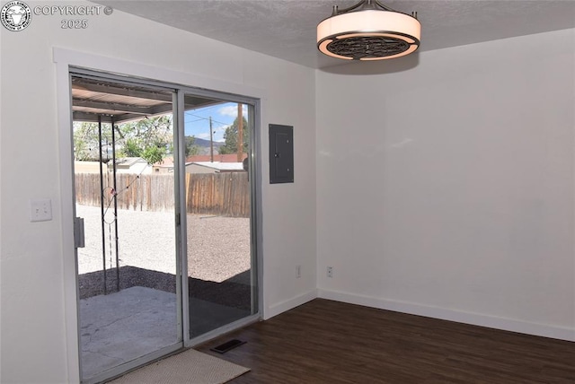 unfurnished dining area featuring electric panel, dark wood-style flooring, a textured ceiling, visible vents, and baseboards