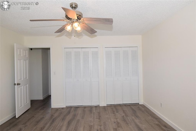 unfurnished bedroom with wood finished floors, baseboards, a textured ceiling, and two closets