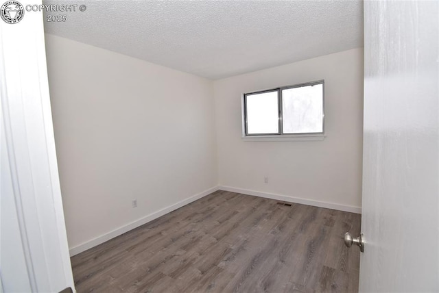 spare room with baseboards, a textured ceiling, visible vents, and wood finished floors