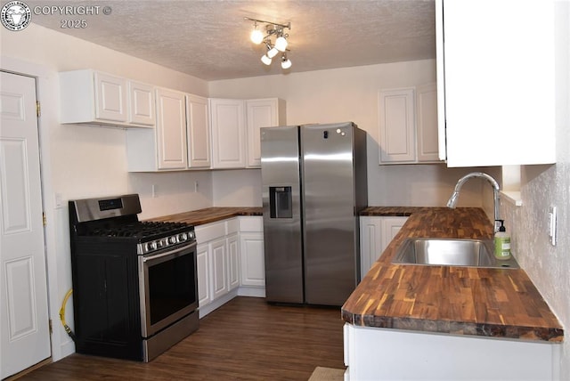 kitchen featuring stainless steel appliances, butcher block counters, a sink, and white cabinetry