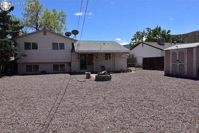 back of property featuring fence, a storage unit, an outdoor fire pit, central AC, and an outbuilding